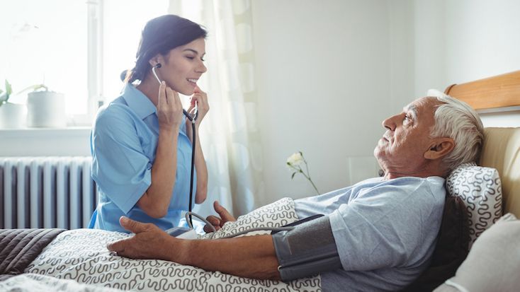 Caregiver using a stethoscope on an elderly patient in a home setting.