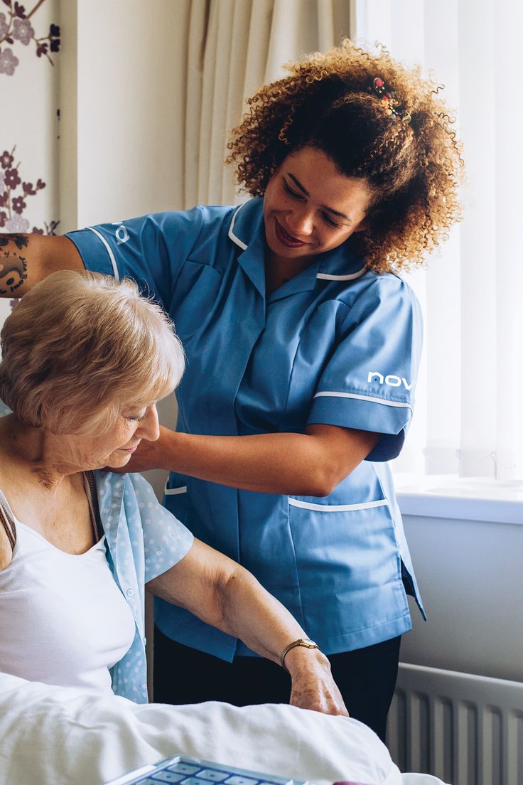 Nurse in blue uniform assisting an elderly patient in bed. Simply Health assistant