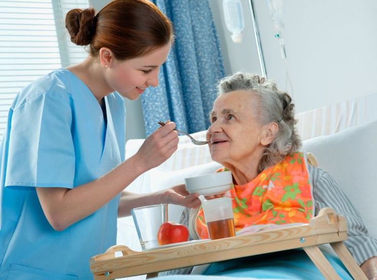 Health care Nurse feeding an elderly patient in a hospital room.